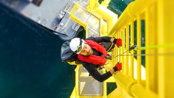 Offshore arbetare klättrar på en stege ute på en oljeplattform  