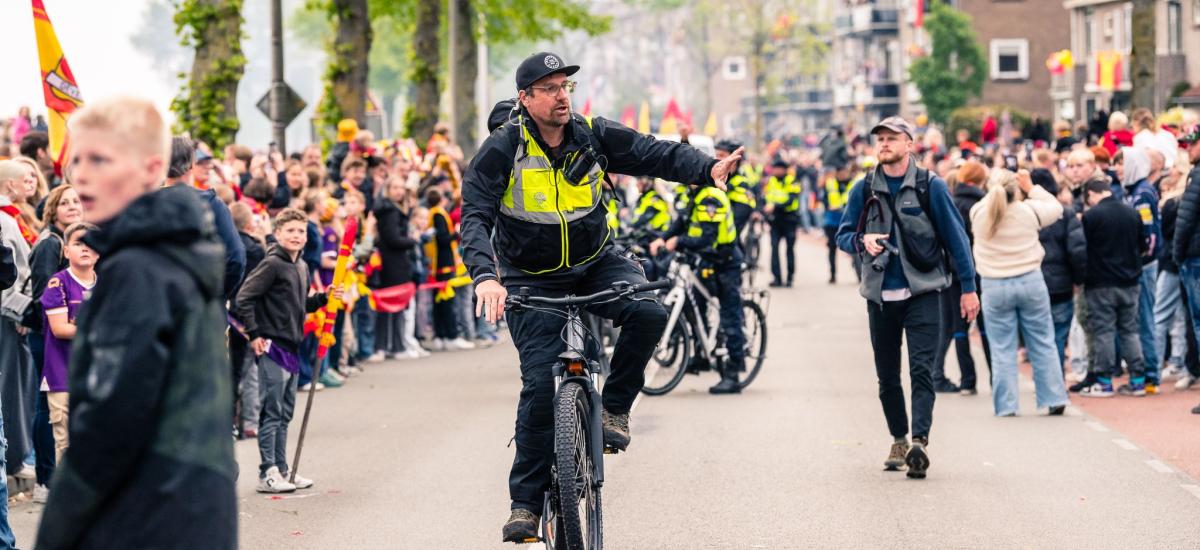 Väktare som cyklar bredvid en lång kö av människor.