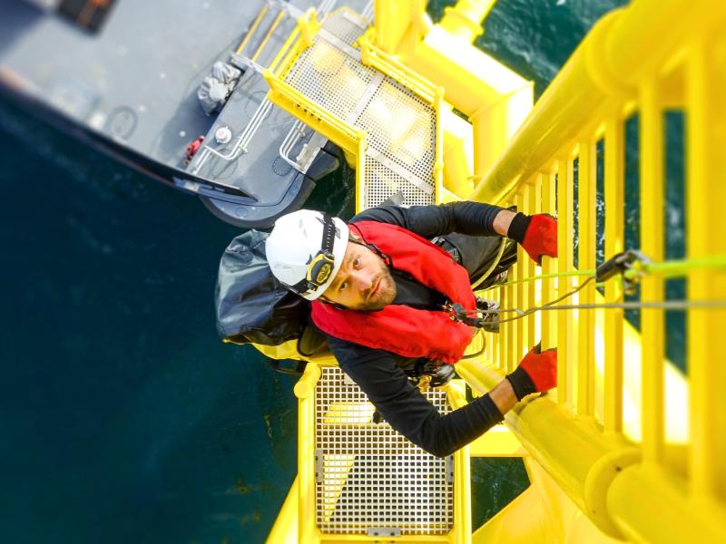 Offshore arbetare klättrar på en stege ute på en oljeplattform  