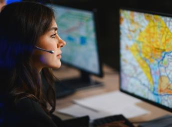 Kvinnlig yrkesperson som arbetar i en larmcentral med headset och övervakar en detaljerad karta på en datorskärm.