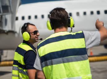 Flygplatsarbetare bär Peltor-hörselskydd med push to talk.